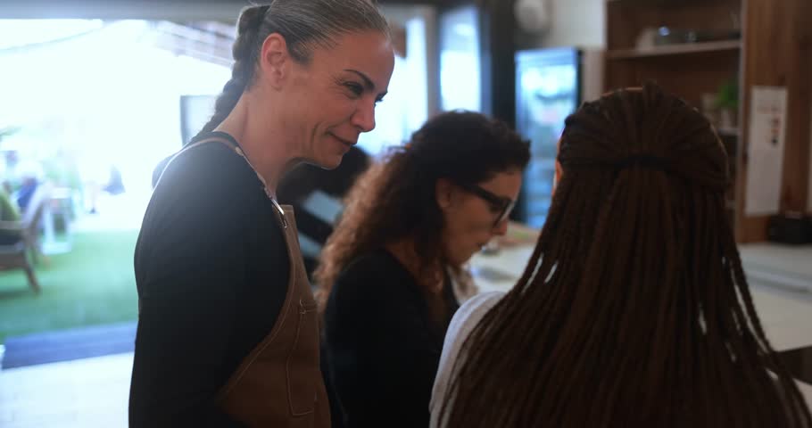 Multiracial women eating lunch together inside brunch bar while talking with joyful waitress - Healthy food, friendship and people lifestyle concept