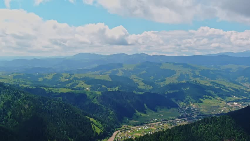 Aerial view of rolling Carpathian Mountains and valley village under summer sky, Ukraine