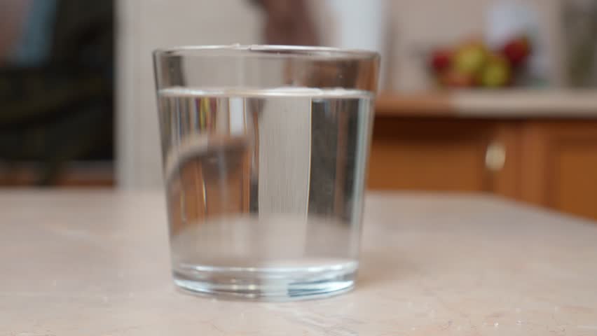 Effervescent aspirin tablet dissolving in a glass of water on a kitchen table, creating bubbles and fizz as it provides pain relief for a headache or hangover cure in a close-up view