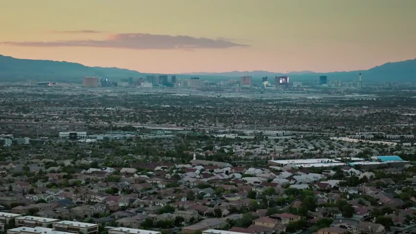 Las Vegas cityscape at sunset with mountains and residential areas in the foreground, showcasing urban expansion and scenic desert views.