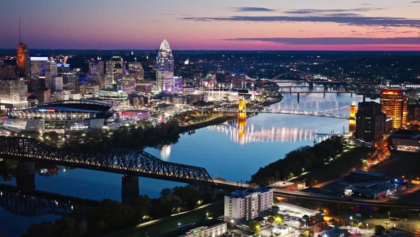 Illuminated Cincinnati skyline at night with bridges over the Ohio River, showcasing vibrant city lights and stunning urban nightscape reflections.