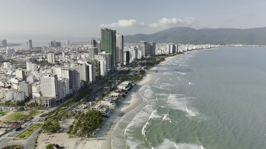 My Khe Beach, Da Nang, Vietnam – 4K aerial drone footage of tropical coastline, sandy beach, palm-lined coastline, ocean waves, and modern city skyline, costal roads, Son Tra Peninsula