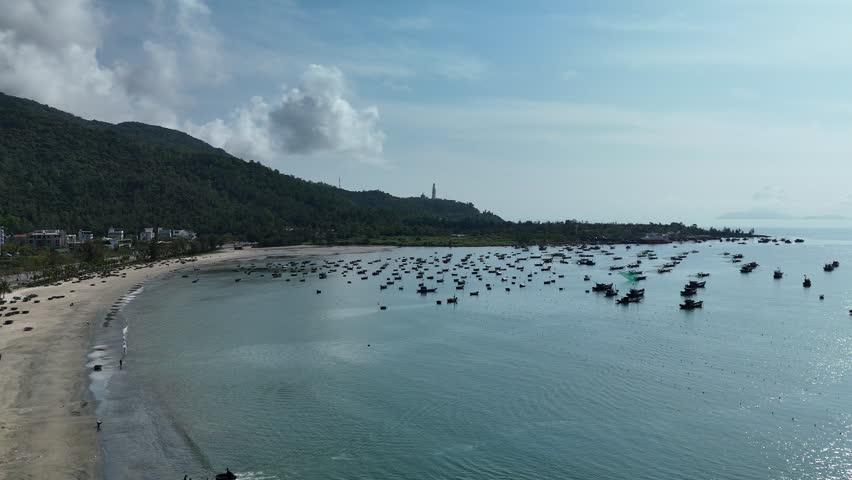 Son Tra Beach, Da Nang, Vietnam – 4K aerial drone footage of curved coastline, fishing boats with Vietnamese flag, fishing village, mountain backdrop and coastal city skyline in the morning