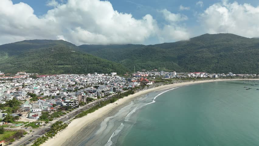 Son Tra Beach, Da Nang, Vietnam – 4K aerial drone footage of curved coastline, fishing boats with Vietnamese flag, fishing village, mountain backdrop and coastal city skyline in the morning