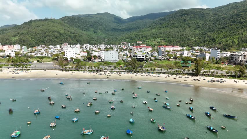 Son Tra Beach, Da Nang, Vietnam – 4K aerial drone footage of curved coastline, fishing boats with Vietnamese flag, fishing village, mountain backdrop and coastal city skyline in the morning