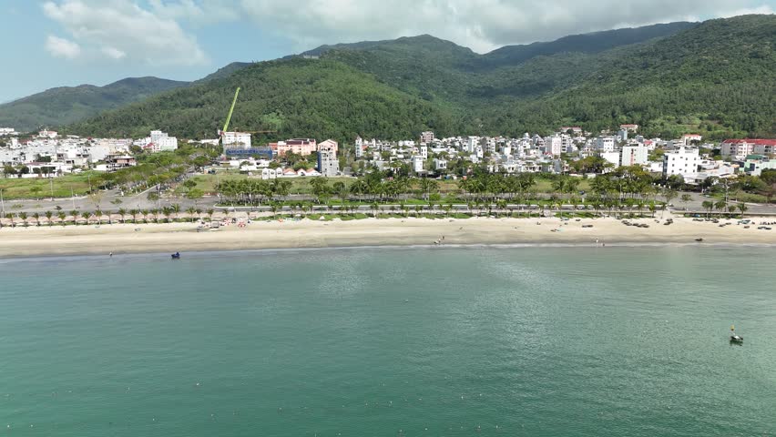 Son Tra Beach, Da Nang, Vietnam – 4K aerial drone footage of curved coastline, fishing boats with Vietnamese flag, fishing village, mountain backdrop and coastal city skyline in the morning