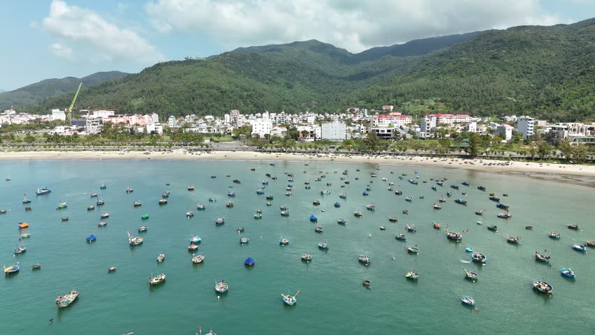Son Tra Beach, Da Nang, Vietnam – 4K aerial drone footage of curved coastline, fishing boats with Vietnamese flag, fishing village, mountain backdrop and coastal city skyline in the morning