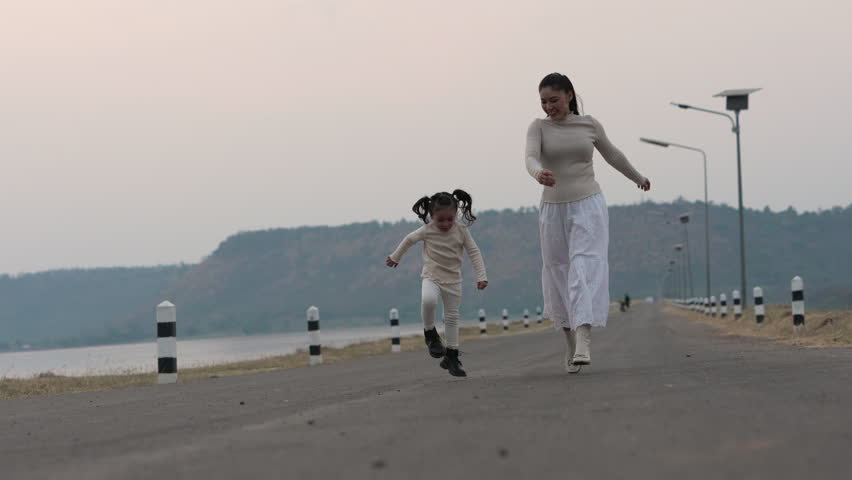 slow motion of Mother and child girl walking and playing on a scenic road during dusk near the river