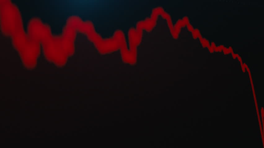 A cinematic close-up of a trading screen where a bright red financial chart is trending sharply downwards against a dark background, symbolizing a major economic crash