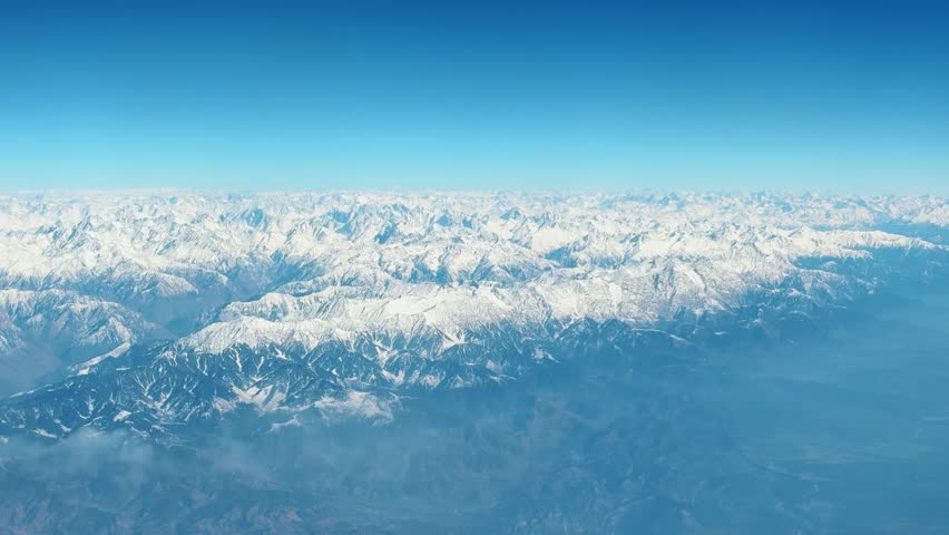 4K aerial shot of winter mountains covered in snow as seen from moving airplane above Kashmir, India. Aerial view of the Himalayas Mountains from an airplane window. Winter nature background. 