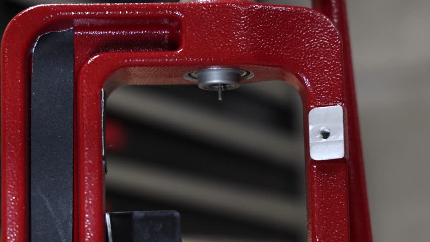 A person's hand is seen adjusting a bolt on a sturdy red reloading press, highlighting the intricate details of firearm ammunition crafting