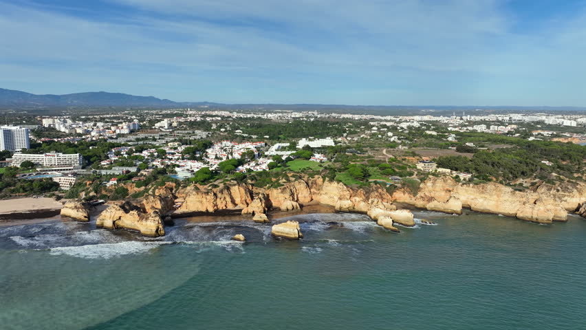View of a European coastal beach in the Algarve, Portugal, with cliffs, rock formations and the Atlantic Ocean along the shoreline.