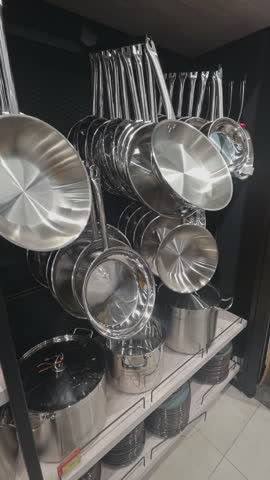 Stainless steel cookware collection displayed in kitchen store, Organized metal pots and pans hanging neatly in modern retail interior, vertical footage