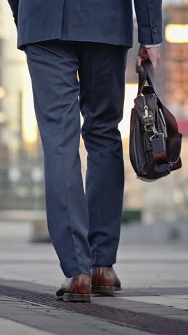Senior businessman with bag walks on street of big city to office building in early morning. Man in blue suit goes to work backside view slow motion
