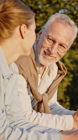 Adult daughter enjoys spending time with elderly father on sunny summer day. Young woman and grey-haired pensioner laugh on walk in part slow motion