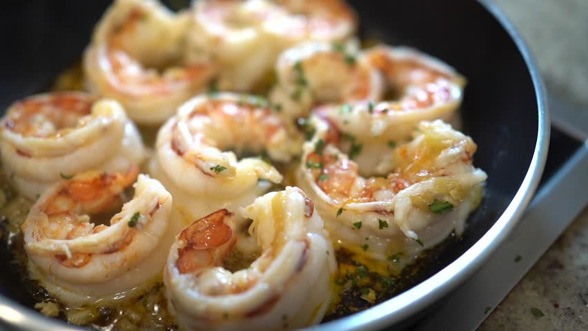 Shrimp sizzling in a hot pan, cooking in a flavorful garlic butter sauce with fresh parsley for a delicious meal