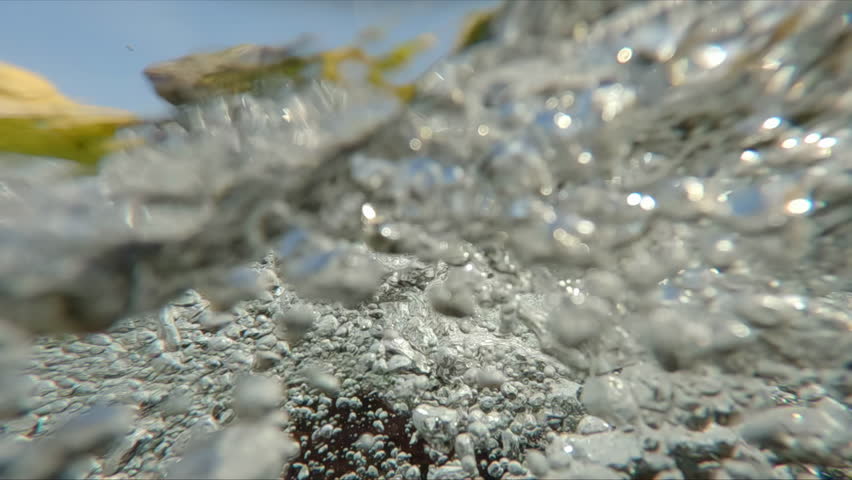 Endless flow of air bubbles under the surface of the water in a mountain stream against blue sky, macro video, super slow motion, Underwater shot, Half water  