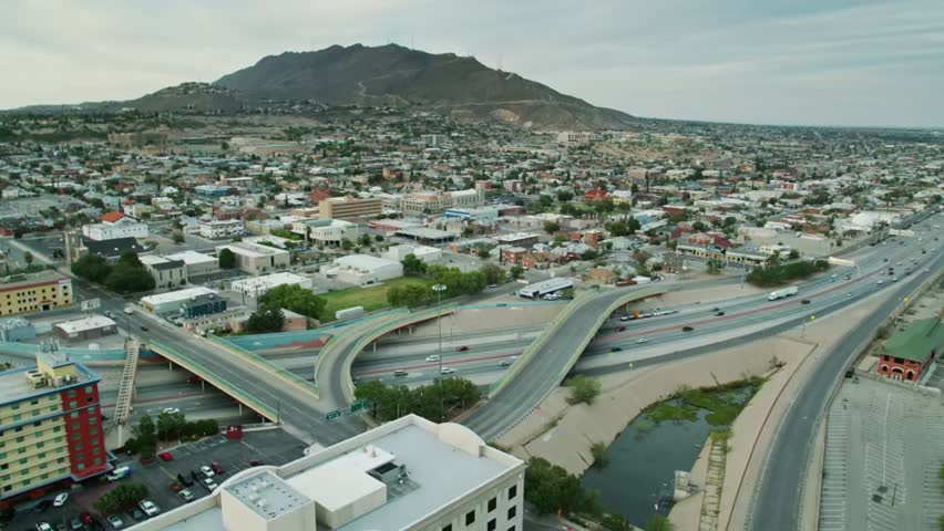 Aerial view of El Paso with busy highways, moving traffic, and rugged mountains in the background, showcasing urban life and landscape.