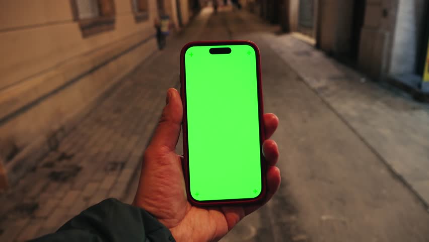 Hand holding smartphone with green screen in street at night, person walking on the street with gadget. High quality 4k footage