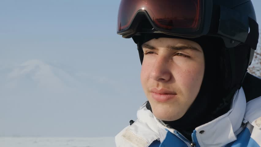 Attractive young skier drinks hot beverage from golden thermos after skiing. Teenage snowboarder happy and satisfied, drinking tea and calmly looking into distance. Copy space.