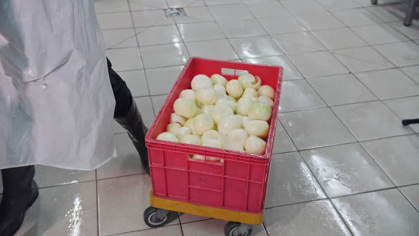 Worker carrying crates of peeled onions in a commercial kitchen.