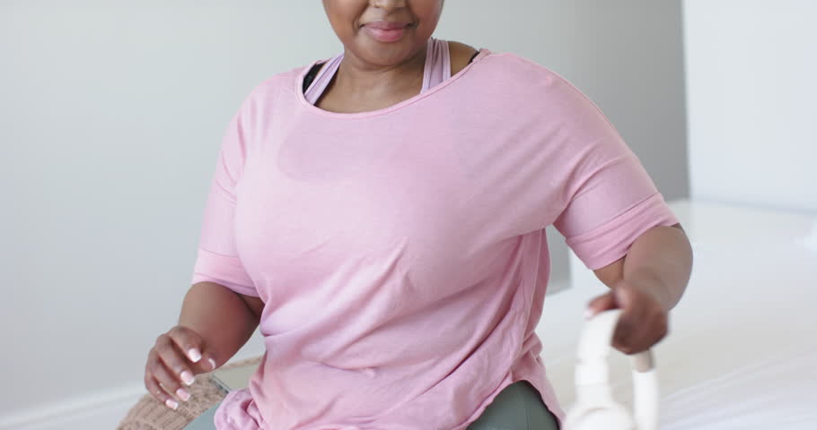 Mid adult African American woman lifting wireless headset at home inspecting and donning for music. Wellness, leisure, serenity, tranquility, modern, fitness, casual