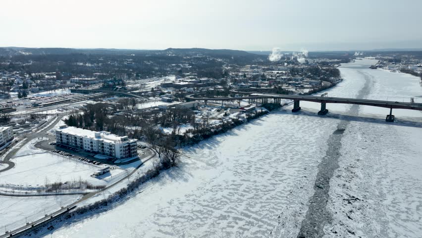 Aerial view of frozen Hudson River in Albany, New York, with bridges, highways, and snowy riverbanks in winter.