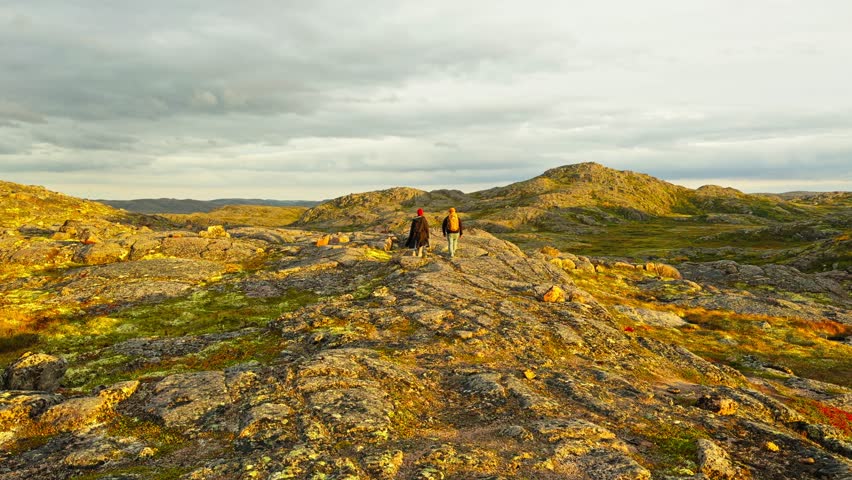 A couple of young people walks along the mountain slopes at sunset, near the Battery waterfall in Teriberka, Russia, Murmansk region, Arctic landscape