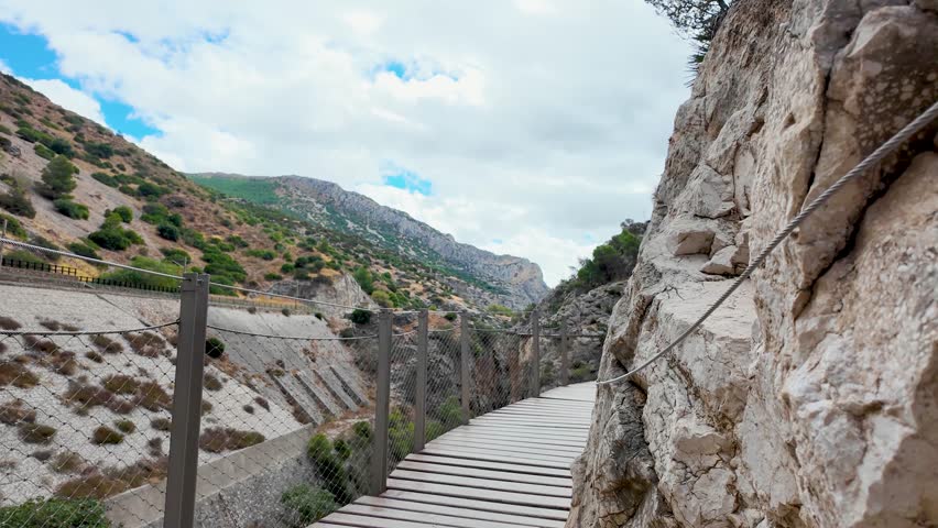 Handheld POV walking shot on the wooden boardwalk of Caminito del Rey in Malaga, showing the narrow path along limestone cliffs and the scenic gorge view.