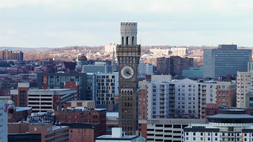 Aerial drone view of downtown Baltimore, with historic clock tower rising above modern residential and office buildings under clear winter sunlight in city skyline. Wide shot. Bromo Seltzer Art tower