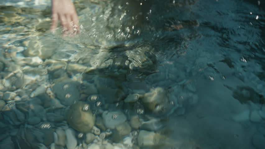 Close up of woman’s hand caressing crystal clear turquoise sea water in Sicily, serene summer Mediterranean detail
