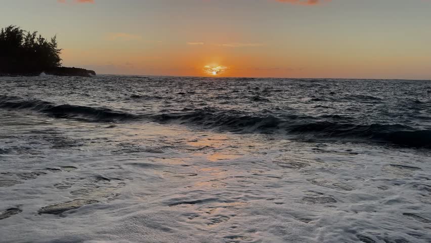 Gentle waves roll onto the shore as the sun rises over the ocean horizon