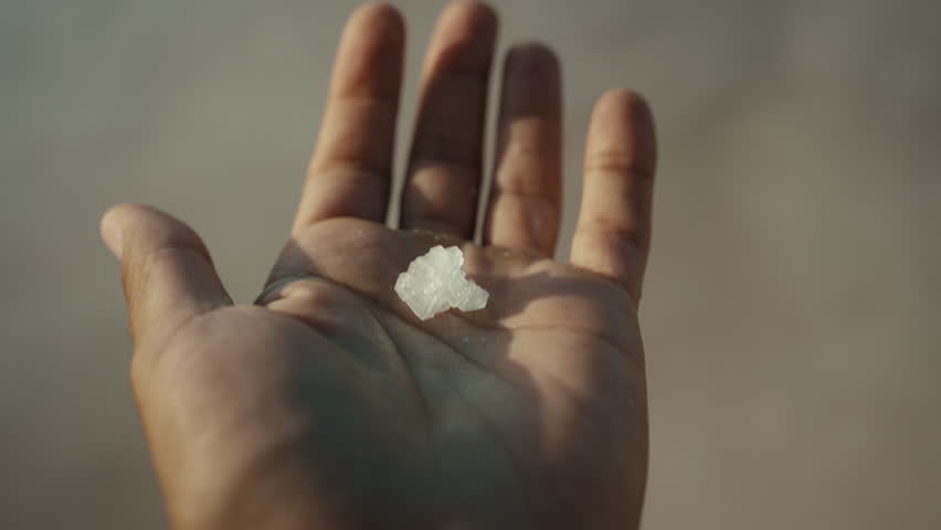 Close up of man’s hand holding a crystal of sea salt at the Marsala salt flats in Sicily, warm summer sunset light