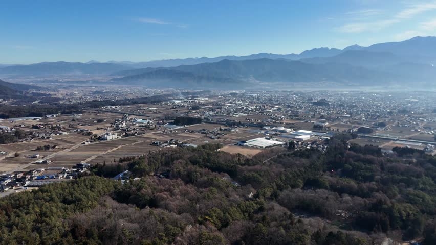 A city with a mountain in the background. The sky is blue and the sun is shining. The city is full of buildings and trees
