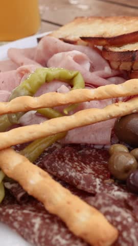 A hand reaches into a vertical frame to grab a breadstick from an antipasto platter.