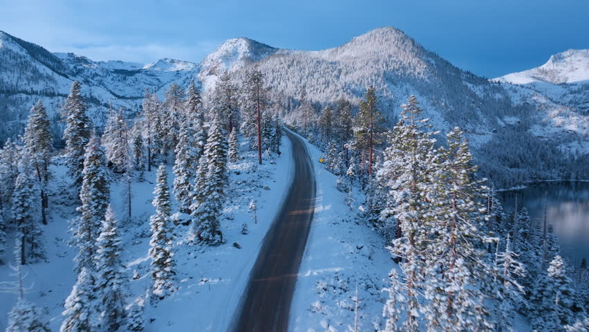 Spectacular sunrise over Emerald Bay Road running along snowy mountain ridge above Lake Tahoe. Golden light reflects on frozen pine forest creating vibrant winter alpine panorama. Lake Tahoe, USA.