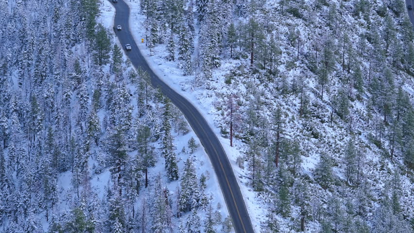 Aerial drone view of winding Emerald Bay Road cutting through snow covered pine forest above Lake Tahoe. Scenic winter drive with alpine trees and fresh snow. Emerald Bay, Lake Tahoe, California, USA.