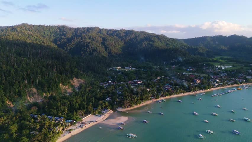 A cinematic aerial drone shot of Port Barton in Palawan, Philippines island , showcasing the tranquil bay filled with traditional bangka boats against a backdrop of lush tropical hills