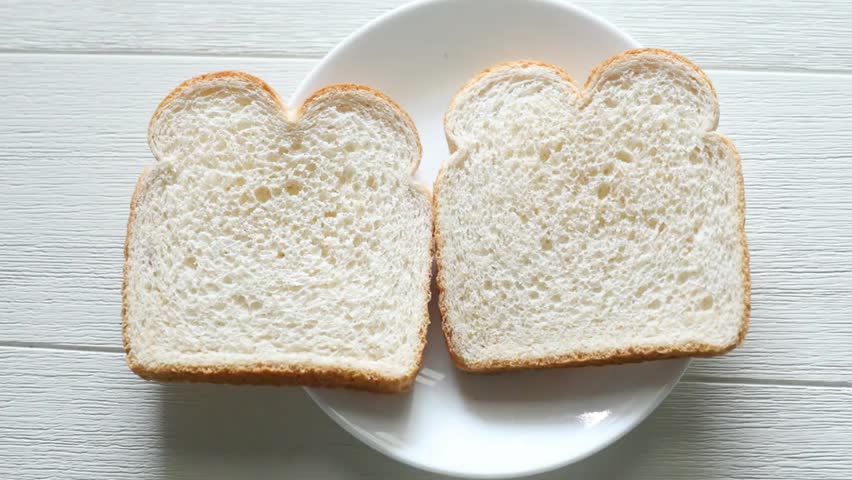Close-up of white bread slices topped with cheese and ham on a white plate, placed on a wooden table in a simple home kitchen setting.
