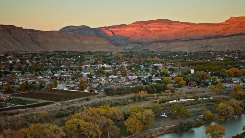 Aerial view of a small town nestled in a scenic valley at sunset, surrounded by mountains and warm golden light across rooftops and landscape.