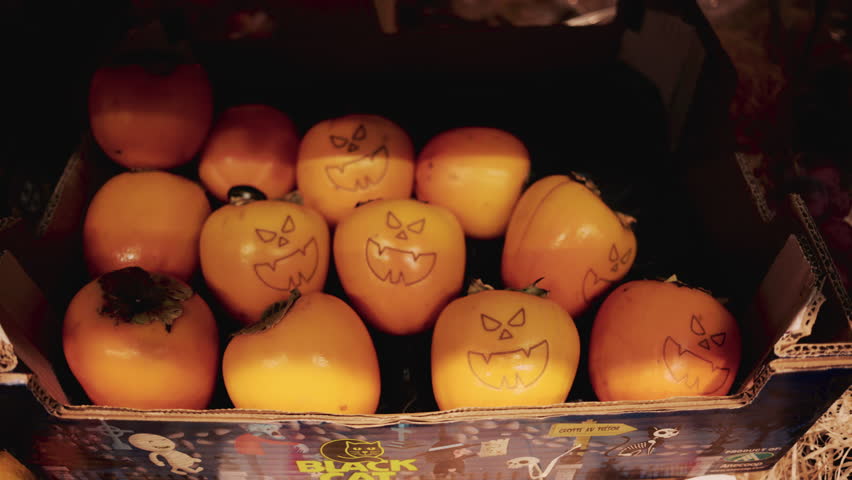 Hand holding a persimmon with a Halloween style jack o