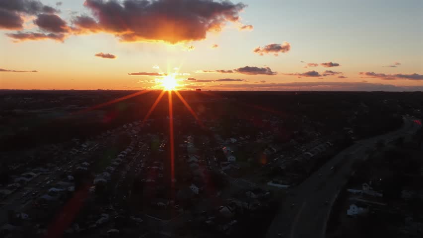 Peaceful orange sunset over quiet suburb neighborhood in America. Aerial lateral wide shot. Houses and homes in rural area of city. Forest landscape in distance.