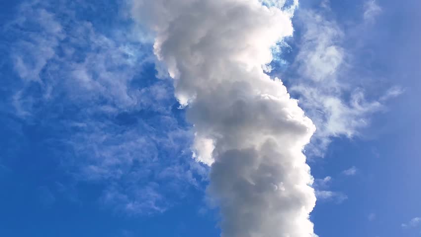 A dense plume of white industrial smoke rises vertically against a bright blue sky.