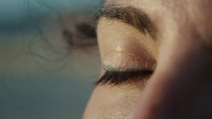 Macro close up of woman opening her eye at sunset on Sicily beach, wind in hair, gazing toward horizon, cinematic summer moment
