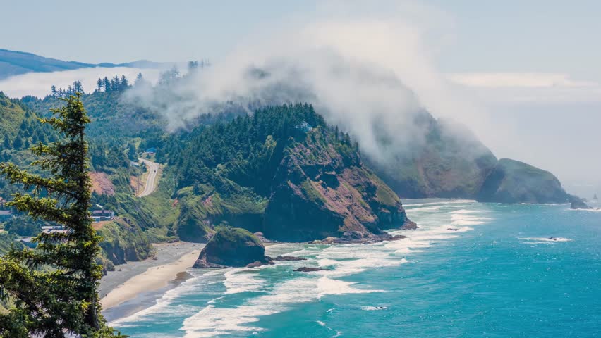 Footage captures a stunning, high-angle view of the dramatic Oregon coastline. Rugged cliffs covered in lush evergreen forests meet the deep blue Pacific Ocean, with white waves crashing onto a seclud