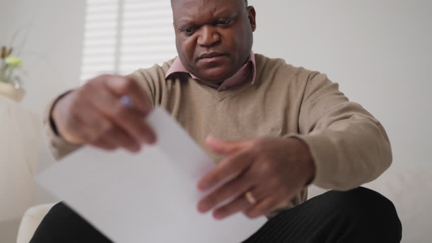 African american homeowner checking utility bills and tax return, portrait. Black man with eyeglasses reading agreements and counting credit payments in apartment, professional insurance agent