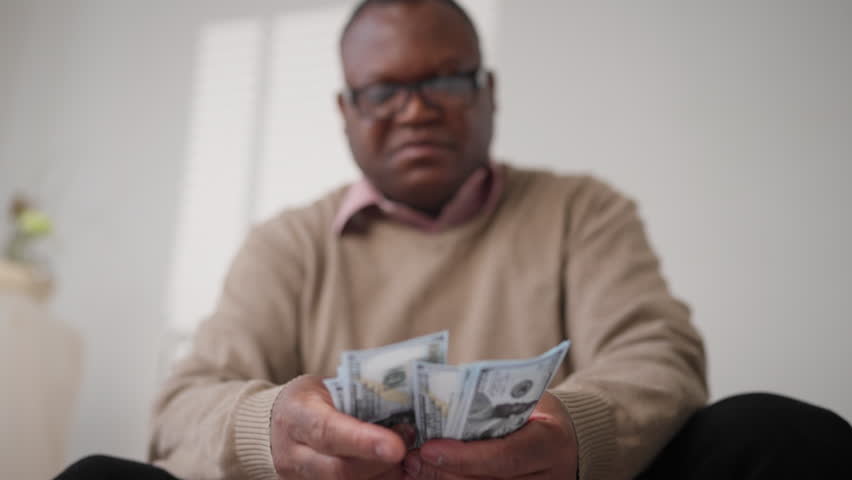 Senior black man counting cash dollars banknotes, planning budget and expenses. Rich male person holding money in hands, portrait in home interior, incomes and salary, save money and control payment