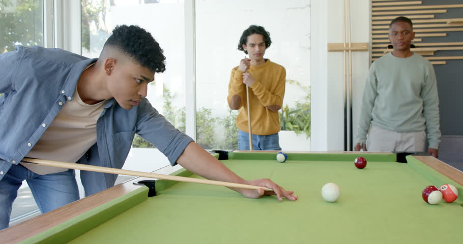 Male player spotting shot, leaning over home pool table, striking cue ball to pocket red balls. Billiards, recreational, modern, social, friendship, competition, leisure