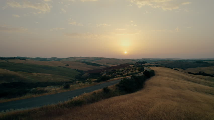 Aerial view of a winding road through golden rolling hills during sunset, showcasing a serene natural landscape.