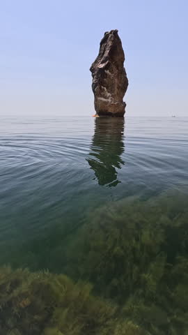 Sea stack, clear water, ocean view, serene rock formation under blue sky. Vertical video.